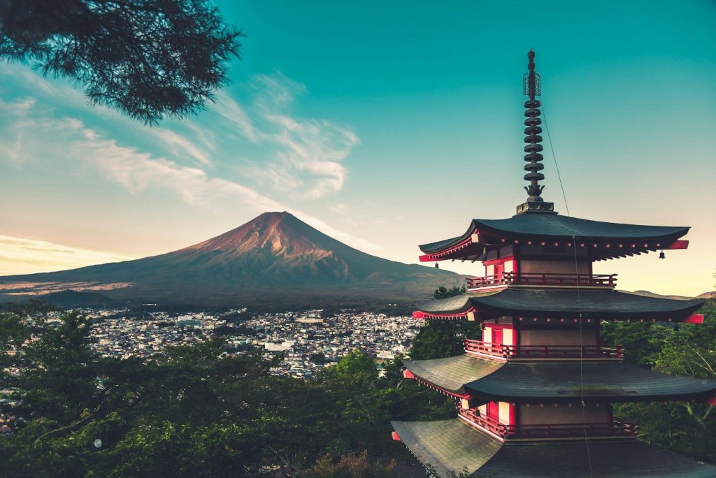 A red pagoda overlooking a city with Mount Fuji in the distance